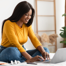 Woman in a yellow shirt working on a laptop.