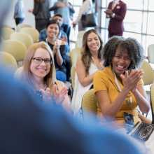 Audience members clapping with smiling at a keynote presenter.
