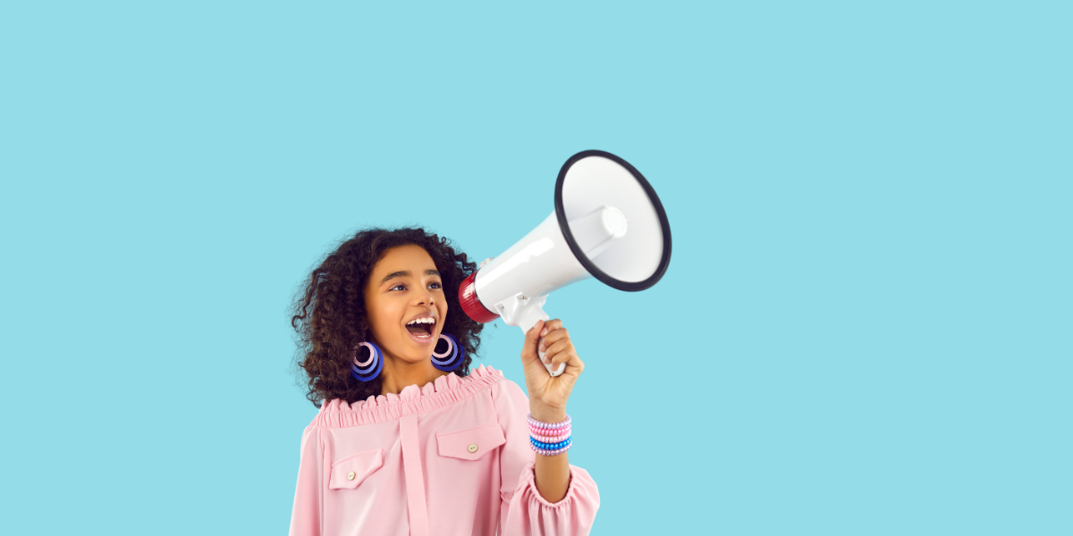 A preteen girl with curly hair in a pink shirt speaking into a red and white megaphone.