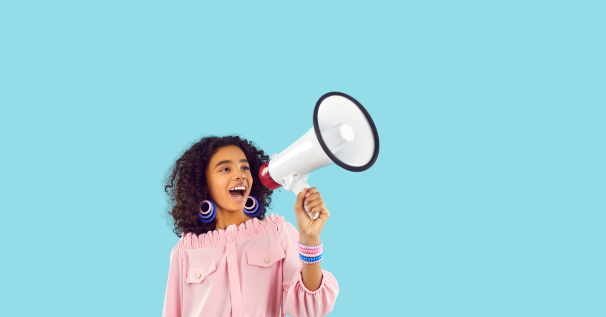 A preteen girl with curly hair in a pink shirt speaking into a red and white megaphone.