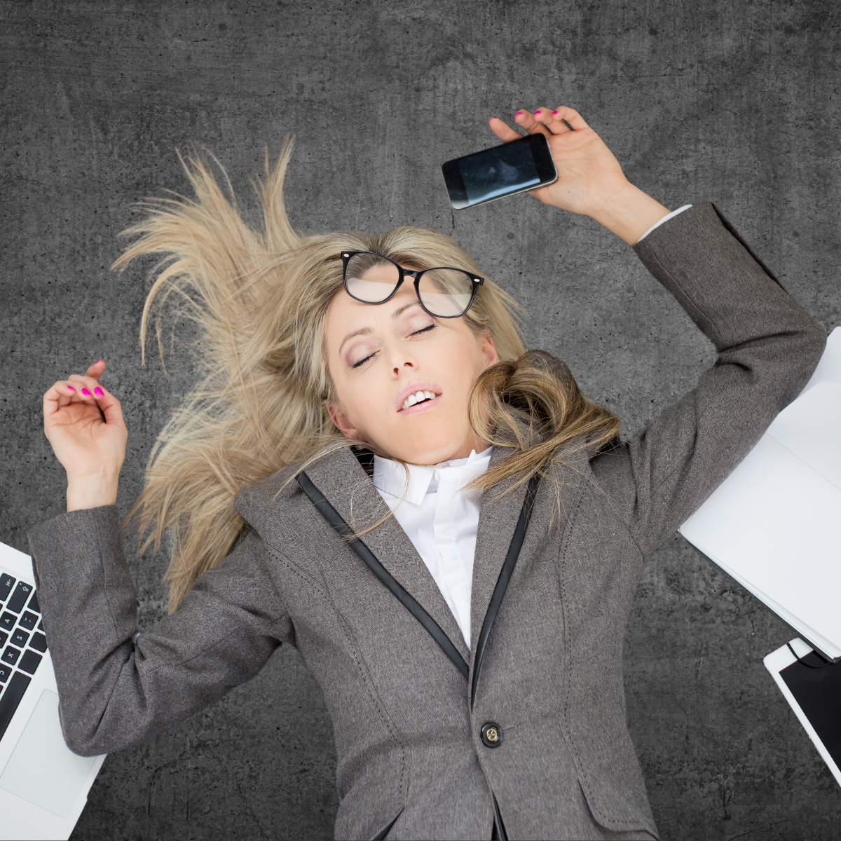 Frazzled professional passed out on the floor with laptop, phone and tablet surrounding her.